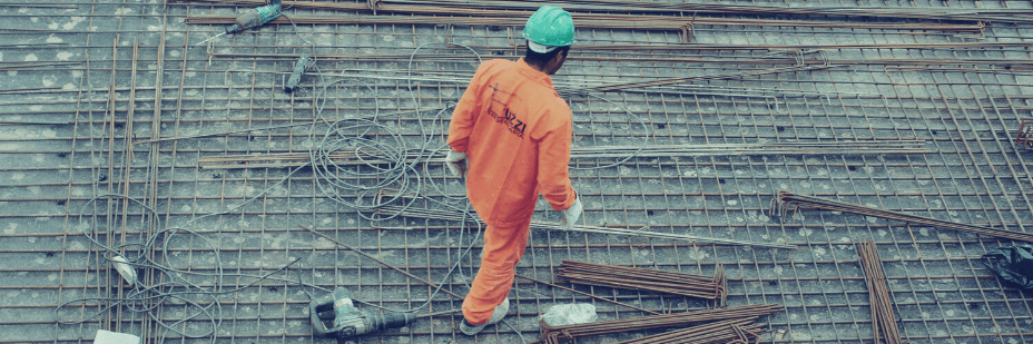 Un ouvrier vue de haut marche sur un chantier avec sa combi orange et son casque vert